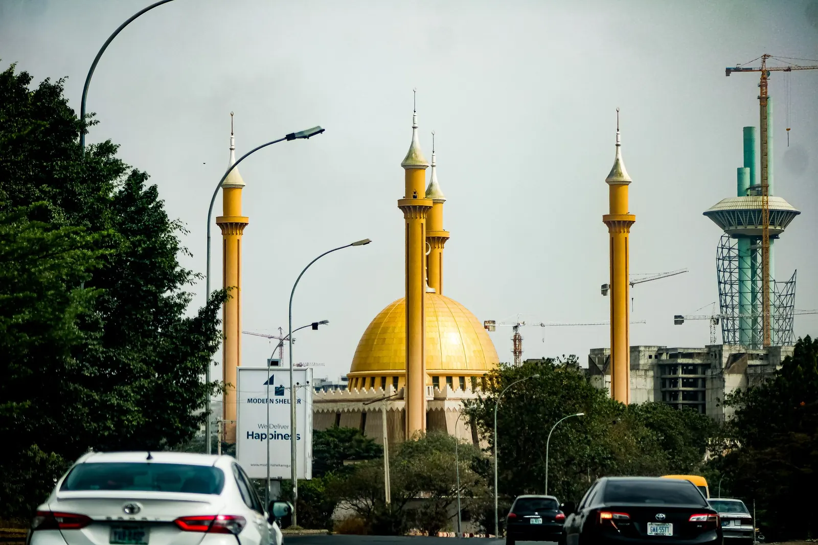The golden dome and minarets of Abuja's National Mosque, with the Millennium Tower behind, seen from a city street